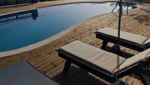 Una piscina con cubierta de madera y sillas de descanso, rodeada de vistas panorámicas a colinas y un cielo despejado.
