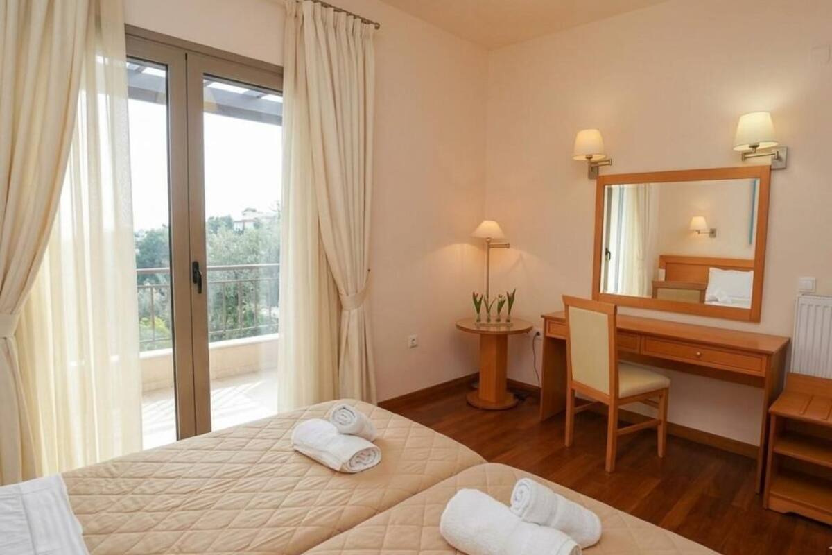 Ein Hotelzimmer mit zwei Betten, einem Schreibtisch, einem Stuhl, einem Spiegel und einem Balkon mit Vorhängen.