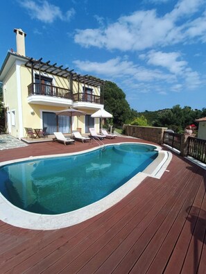 Ein Pool mit Liegestühlen und Sonnenschirmen, ein Gebäude mit Balkon und ein klarer Himmel.