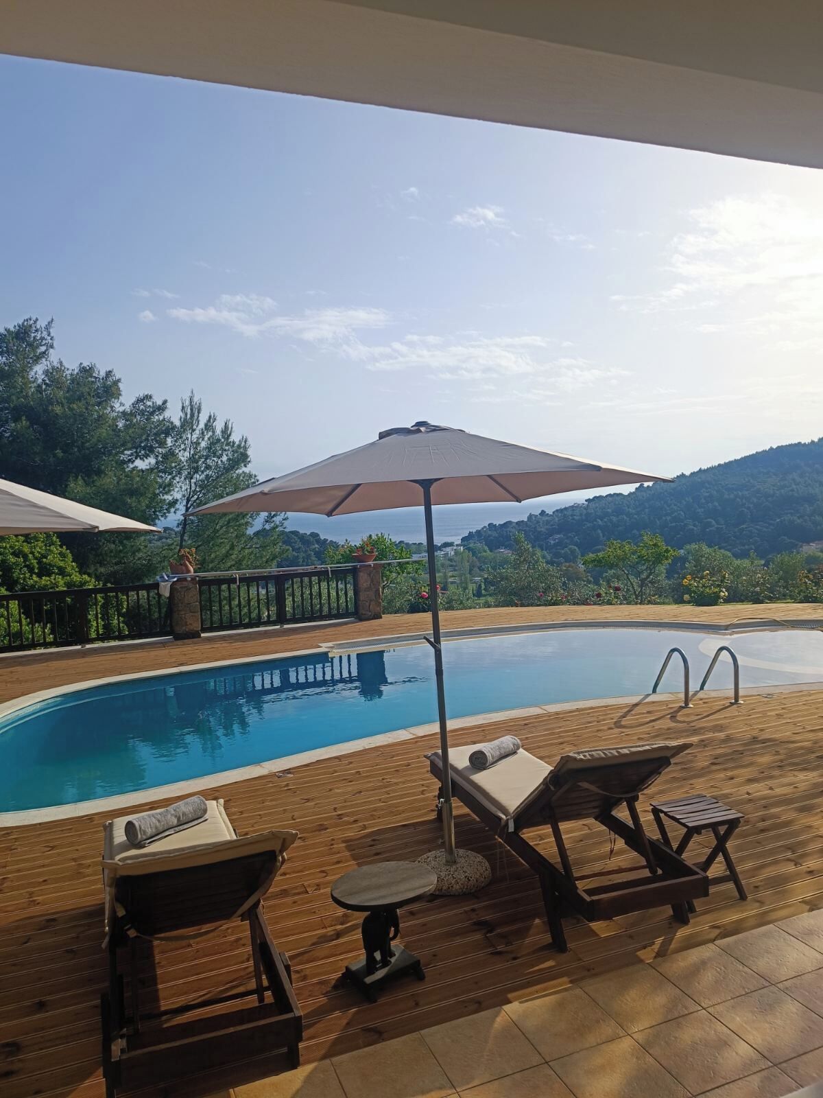 A swimming pool with lounge chairs and an umbrella, surrounded by a wooden deck and a view of the hills.