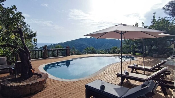 Una terraza de madera con piscina, sillas de descanso y una sombrilla grande.