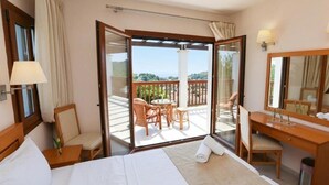 Habitación de hotel con cama, escritorio, silla, una mesita y un balcón con mobiliario exterior.