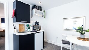 A compact kitchen with a refrigerator, microwave, and coffee maker, a small dining table with chairs, and a framed quote on the wall. - Guestz at The Wellington (Blackpool)
