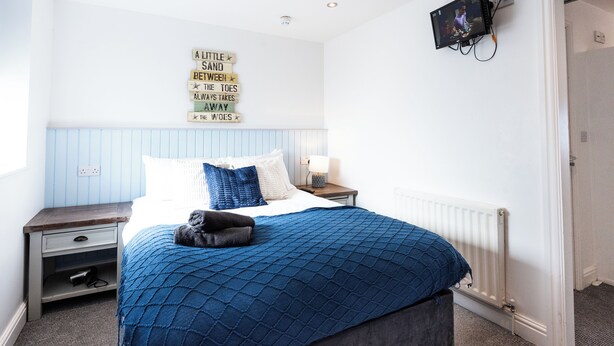 A bedroom with a bed, a nightstand, a wall-mounted TV, and a motivational quote on the wall. - Guestz at The Wellington (Blackpool)