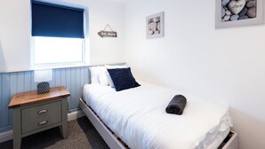 A bedroom with a bed, a bedside table, a window with a blue blind, and wall decorations including a framed picture and a sign. - Guestz at The Wellington (Blackpool)