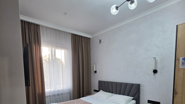 A hotel room with a bed, bedside table, wooden floor, and a ceiling light fixture. - Toi At-Bashy hotel (At-Bashy)