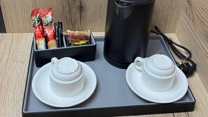 Un plateau avec deux tasses blanches, un thermos noir et une boîte à collation contenant des en-cas et une petite assiette.