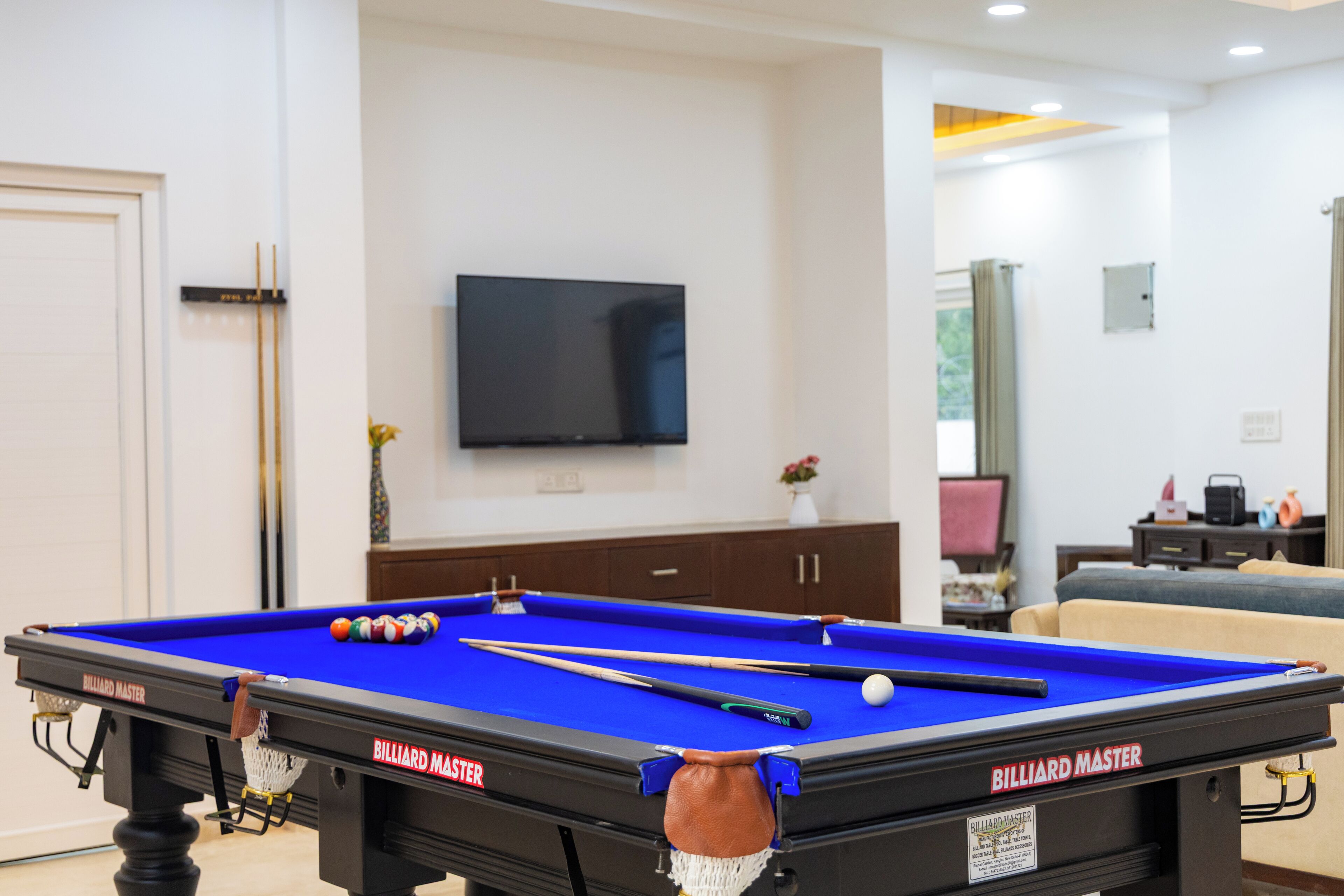 A pool table with billiard cues, a television on the wall, and a sofa in the background.