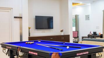 A pool table with billiard cues, a television on the wall, and a sofa in the background.