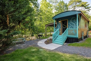 Une petite cabane rustique, dotée d’un porche et d’un escalier, entourée d’arbres.