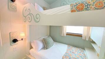 A bunk bed room with a patterned bedspread, wall-mounted lamps, and a window with curtains.