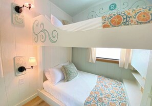 Habitación con literas, colcha estampada, lámparas fijadas a la pared y ventana con cortinas.