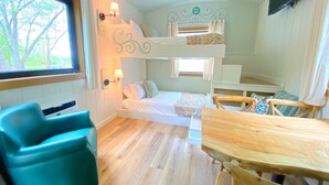 Habitación con literas, una mesa y sillas, una ventana con cortinas y un televisor montado en la pared.
