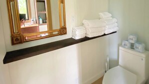 Un baño con inodoro, lavamanos, espejo con marco dorado y estante con toallas dobladas.