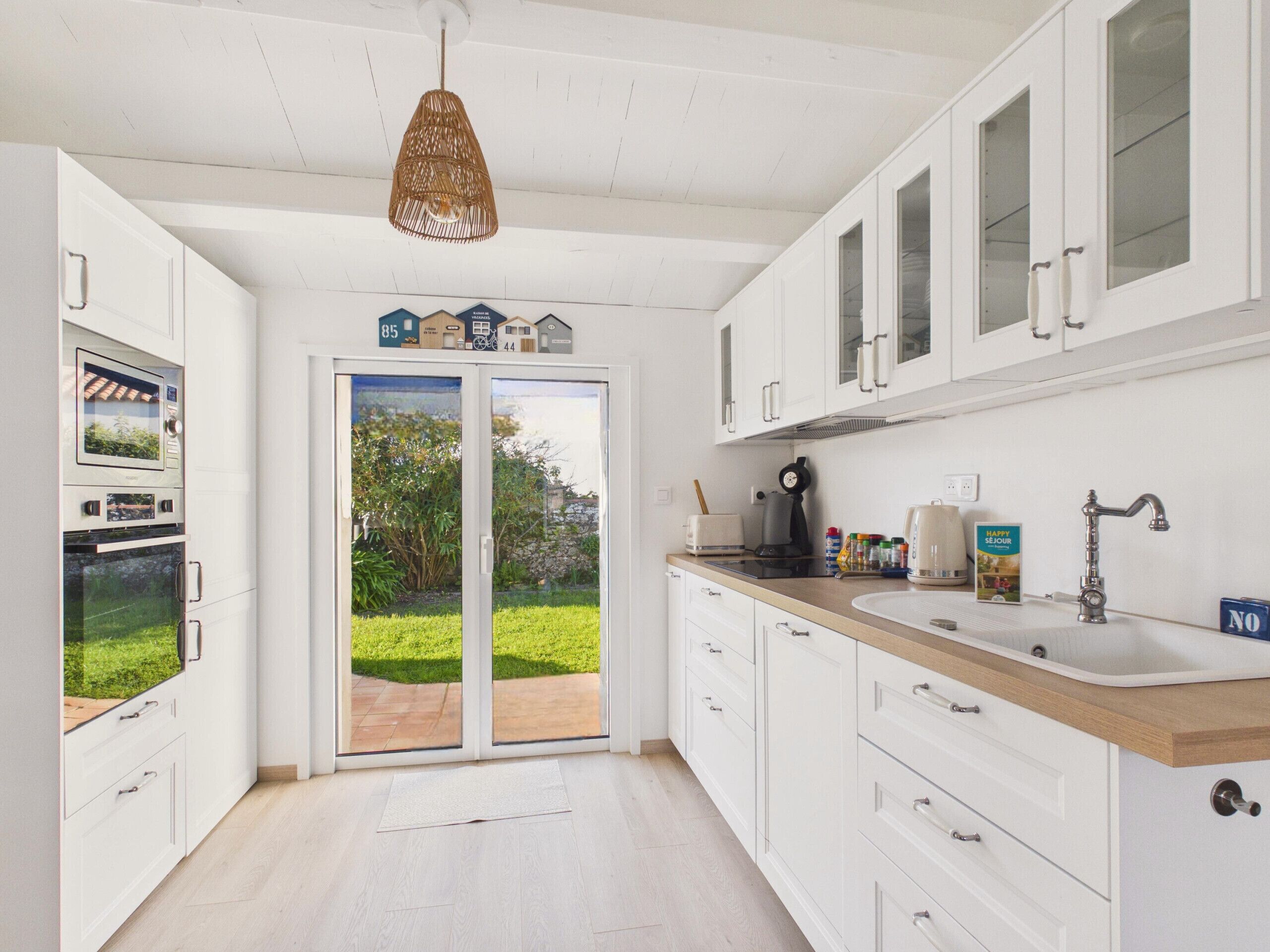 Une cuisine moderne avec des armoires blanches, un plan de travail en bois, un four encastré et une vue sur un jardin, visible à travers des portes vitrées.