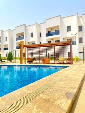 A swimming pool with a pergola and outdoor seating area, surrounded by a multi-story residential building. - Residence541 Apartments and Suites (Abuja)