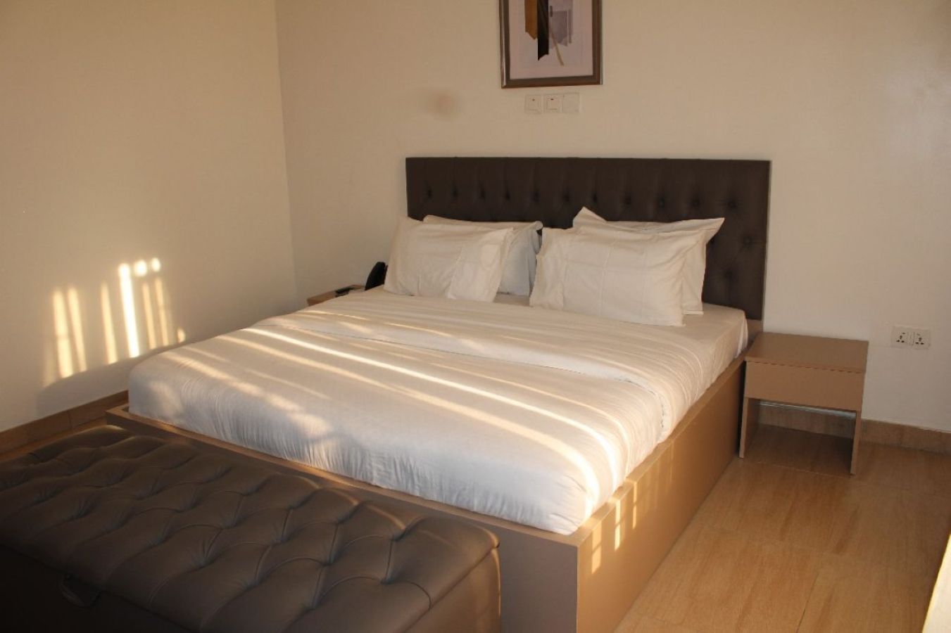 A neatly made bed with a headboard, a bedside table, and a small nightstand.