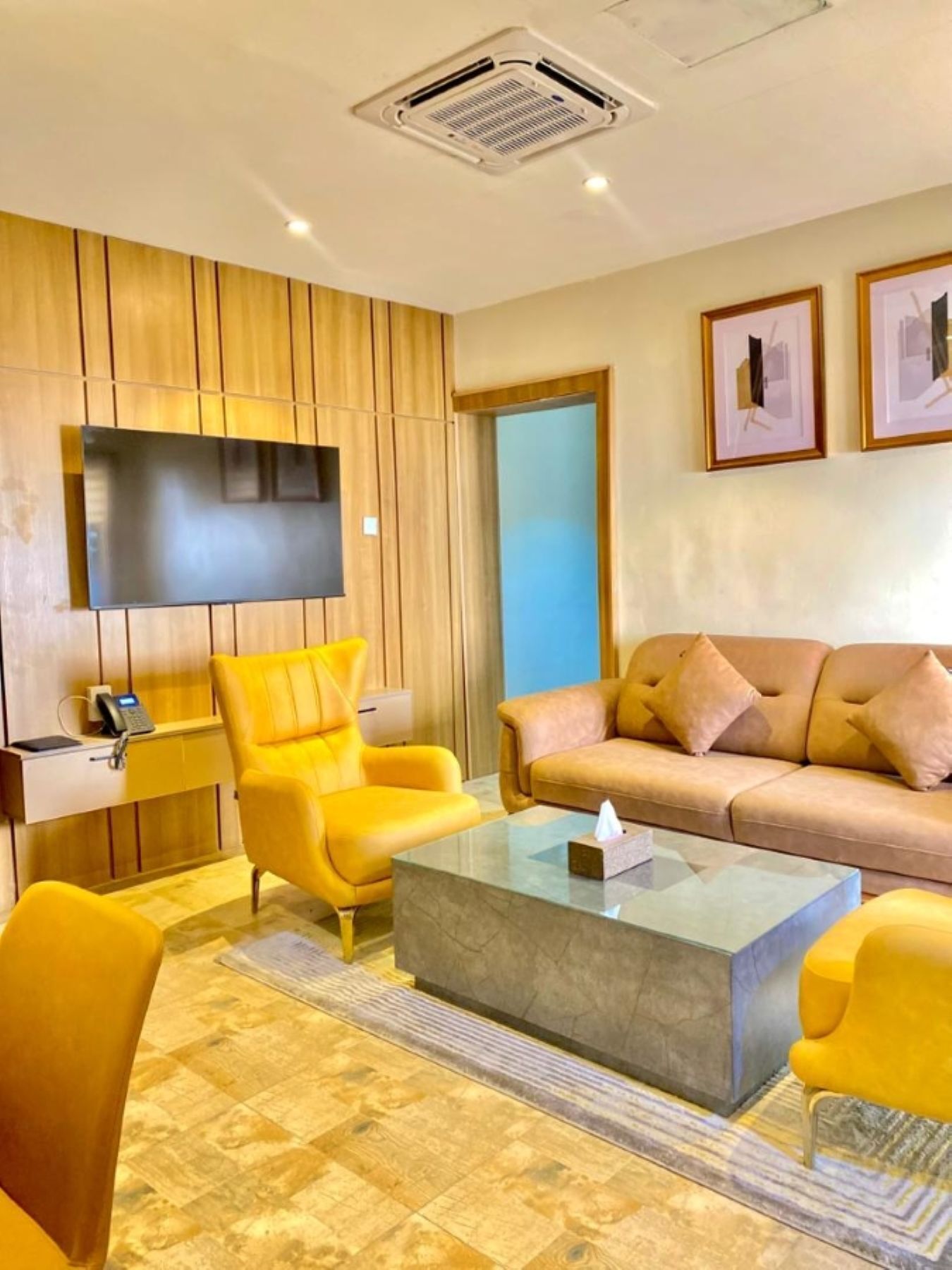 A modern living room with a sofa, armchairs, a coffee table, a flat-screen TV, and a telephone on a desk.