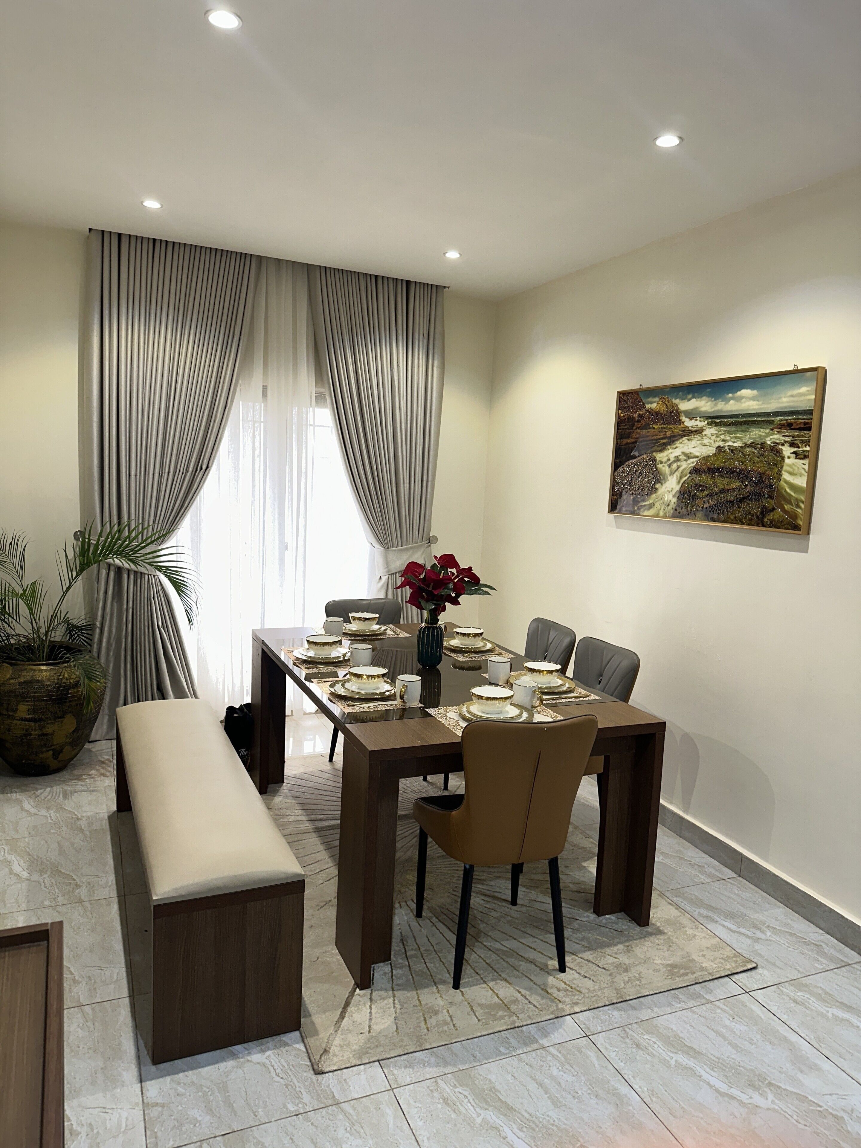 A modern dining room with a long table set for six, a bench, and a painting on the wall.