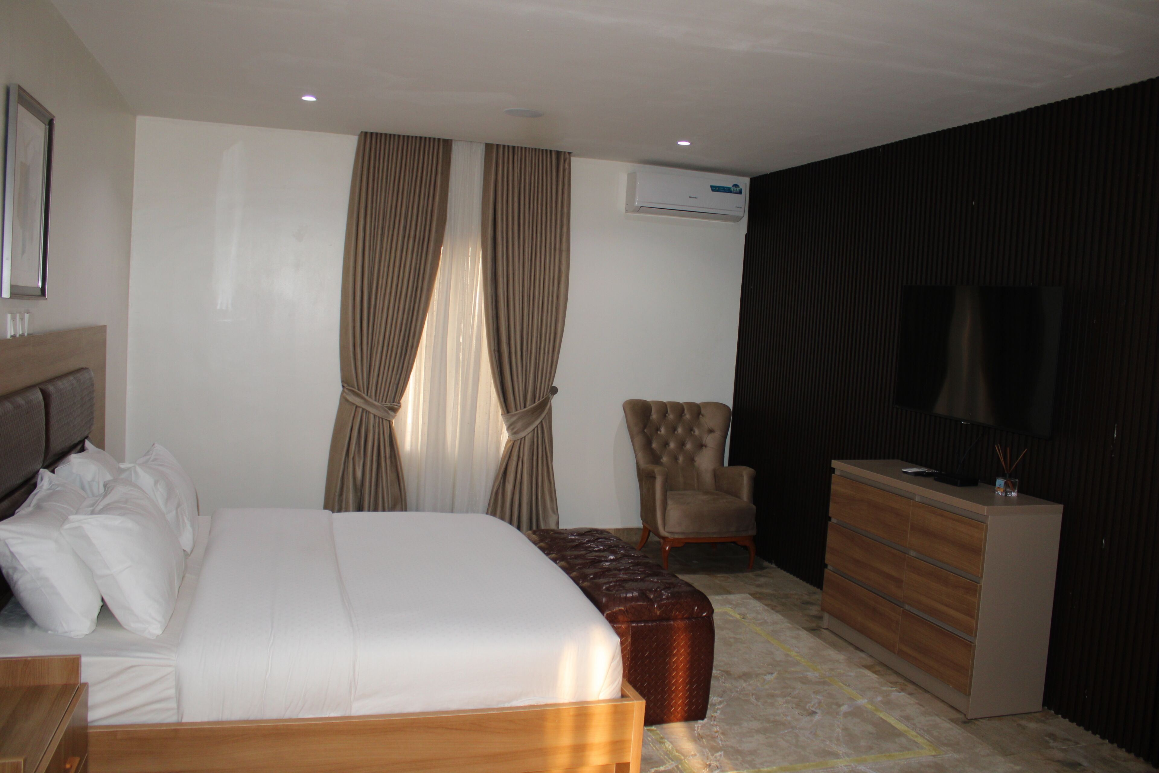 A hotel room with a bed, a chair, a dresser, and an air conditioning unit.