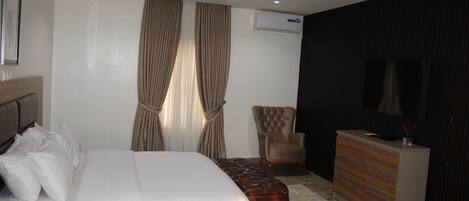 A hotel room with a bed, a chair, a dresser, and an air conditioning unit.