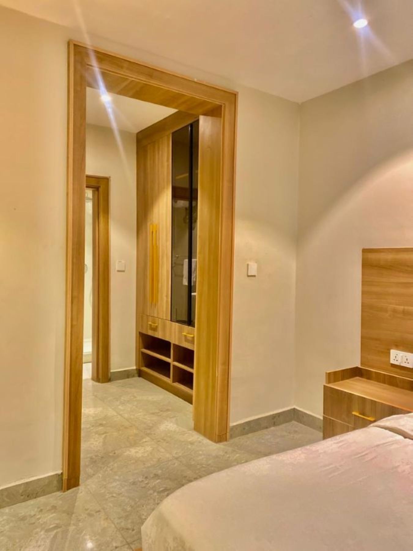 A bedroom with a bed, a wooden wardrobe, a small wooden nightstand, and a mirror.