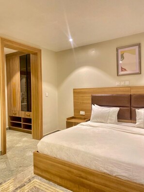 A hotel room with a wooden bed frame, a headboard, a bedside table, and a wardrobe with a mirror. - Residence541 Apartments and Suites (Abuja)