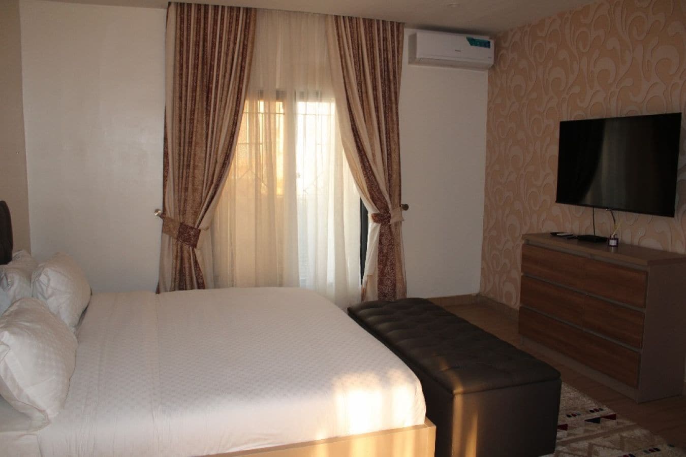 A hotel room with a bed, a television, a dresser, and curtains.