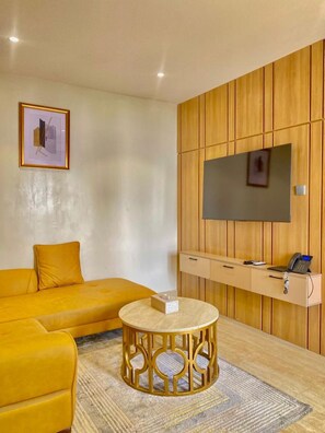 A modern living room with a sofa, a round coffee table, a mounted TV, and a wooden panel wall. - Residence541 Apartments and Suites (Abuja)