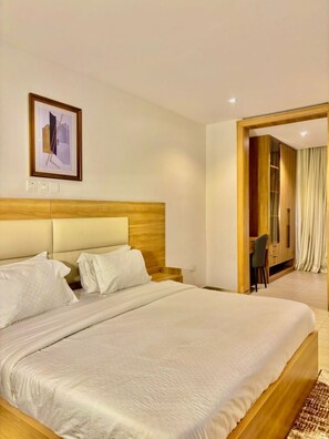 A hotel room with a large bed, a wooden headboard, a desk with a chair, and a wardrobe. - Residence541 Apartments and Suites (Abuja)