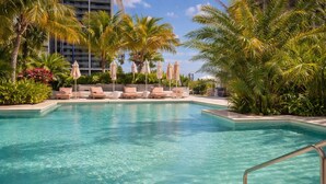 A swimming pool with lounge chairs and umbrellas, surrounded by palm trees and greenery. - RS Suites - Miami World Center (Miami)