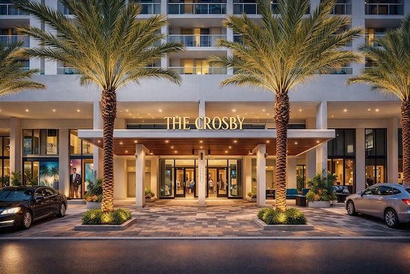 A hotel entrance with palm trees, a covered entrance, and a sign reading 'THE CROSBY.'