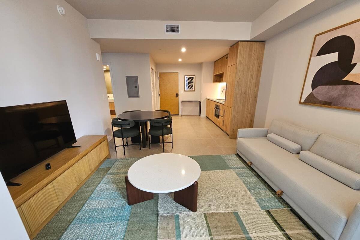 Sala de estar con televisor, sofá, mesa de centro y comedor con sillas.