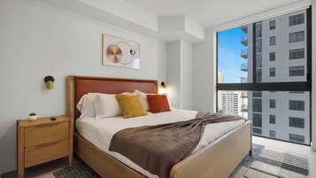 A modern bedroom with a wooden bed, a nightstand, a wall-mounted lamp, and a large window with a city view.