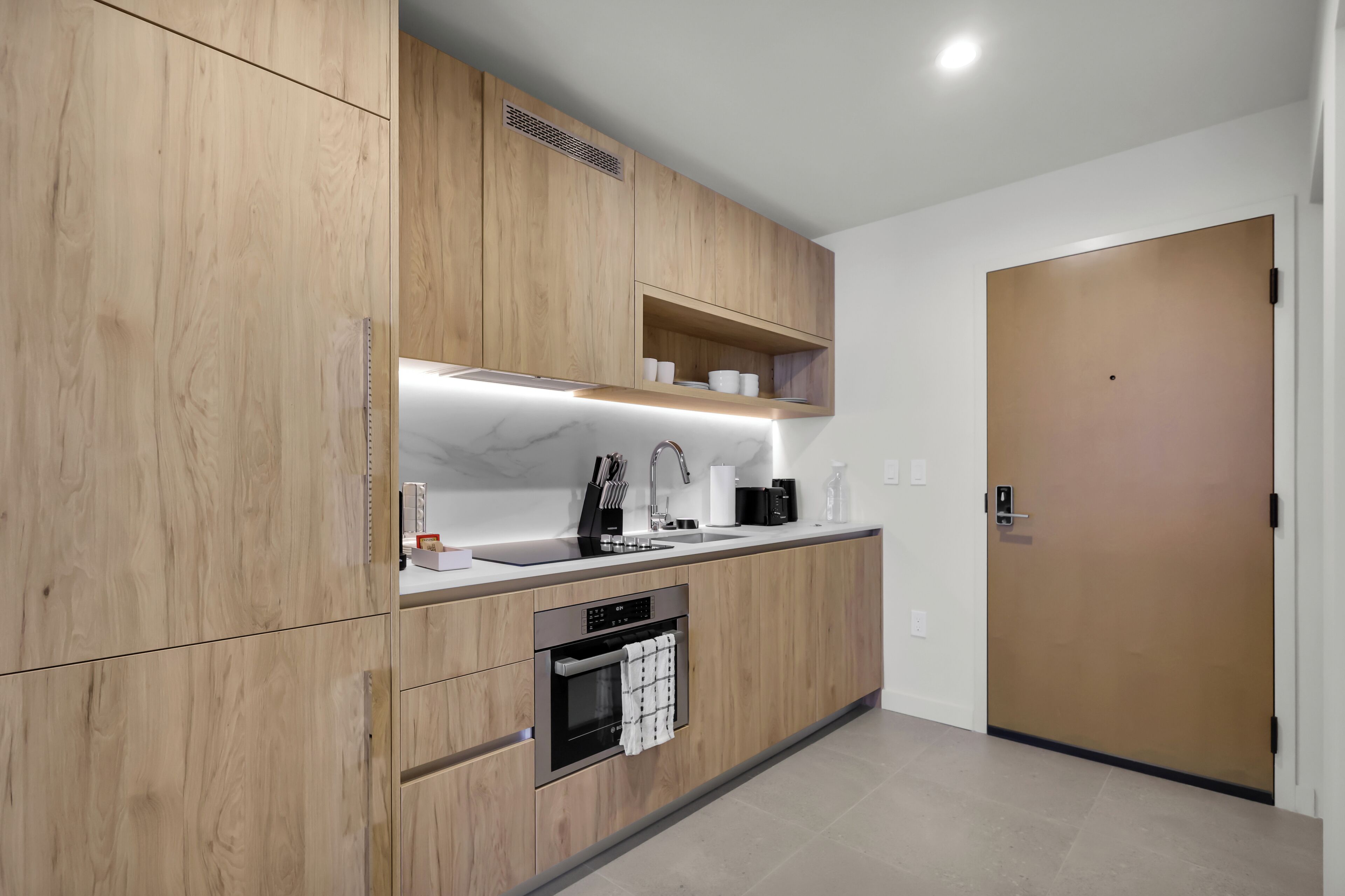 A modern kitchen with wooden cabinets, a built-in oven, a sink, and a countertop with various appliances.
