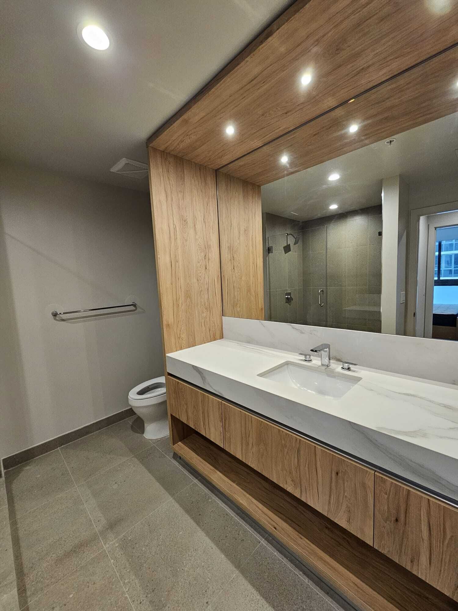 A modern bathroom with a wooden vanity, a large mirror, and a shower enclosure.