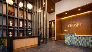 A reception area with a wooden reception desk, a tiled floor, and a wall with shelves displaying various decorative items. - RS Suites - Miami World Center (Miami)
