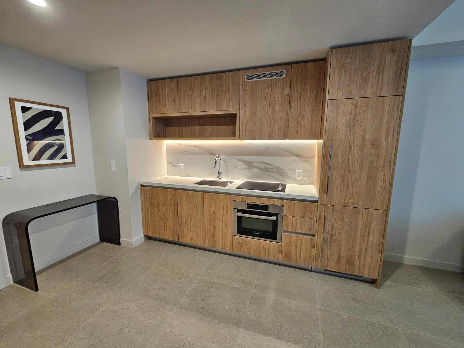 A modern kitchen with wooden cabinetry, a built-in oven, and a marble backsplash.