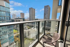 Un balcón con una silla, con vistas a un paisaje urbano de edificios altos y cielo despejado.