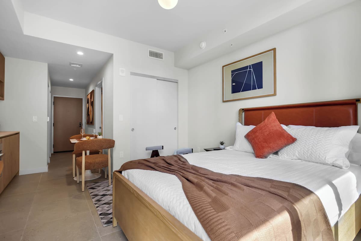 Una habitación de hotel con cama, escritorio, silla, zona de comedor y un pasillo que conduce a otra habitación.