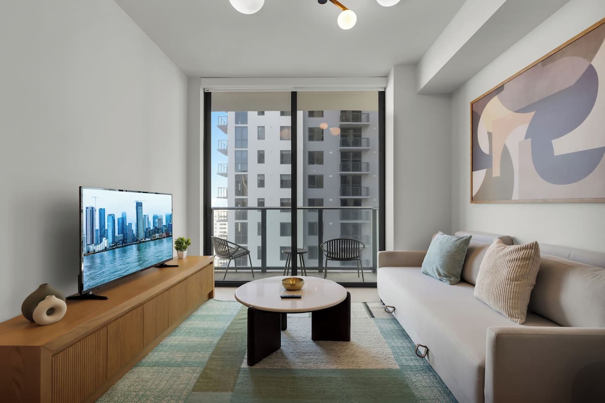 Una sala de estar moderna con un televisor grande, una mesa de centro redonda, un sofá y un balcón con vista a la ciudad.