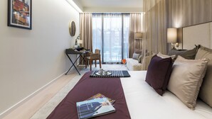 Una camera d'albergo con un letto grande, una scrivania con una sedia, vista sugli edifici dalla finestra e un quadro appeso al muro.