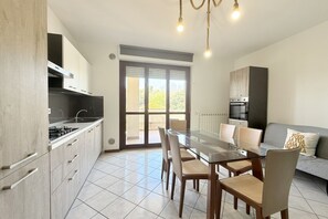 A modern kitchen with a dining area, including a glass table and chairs, a built-in oven, and a view through a glass door. - P088 - Porto Recanati, new three-room apartment with balcony (Porto Recanati)
