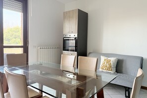 A modern kitchen with a built-in oven and a dining area with a glass table and chairs. - P088 - Porto Recanati, new three-room apartment with balcony (Porto Recanati)