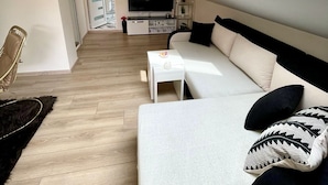 En modern lägenhet i loftstil med högt i tak, ett takfönster, en soffa, en tv och ett litet sidobord.