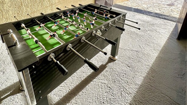 Ett fotbollsspelbord i ett rum med en vägg som har en intressant yta, en darttavla och en dörr med ett geometriskt mönster.
