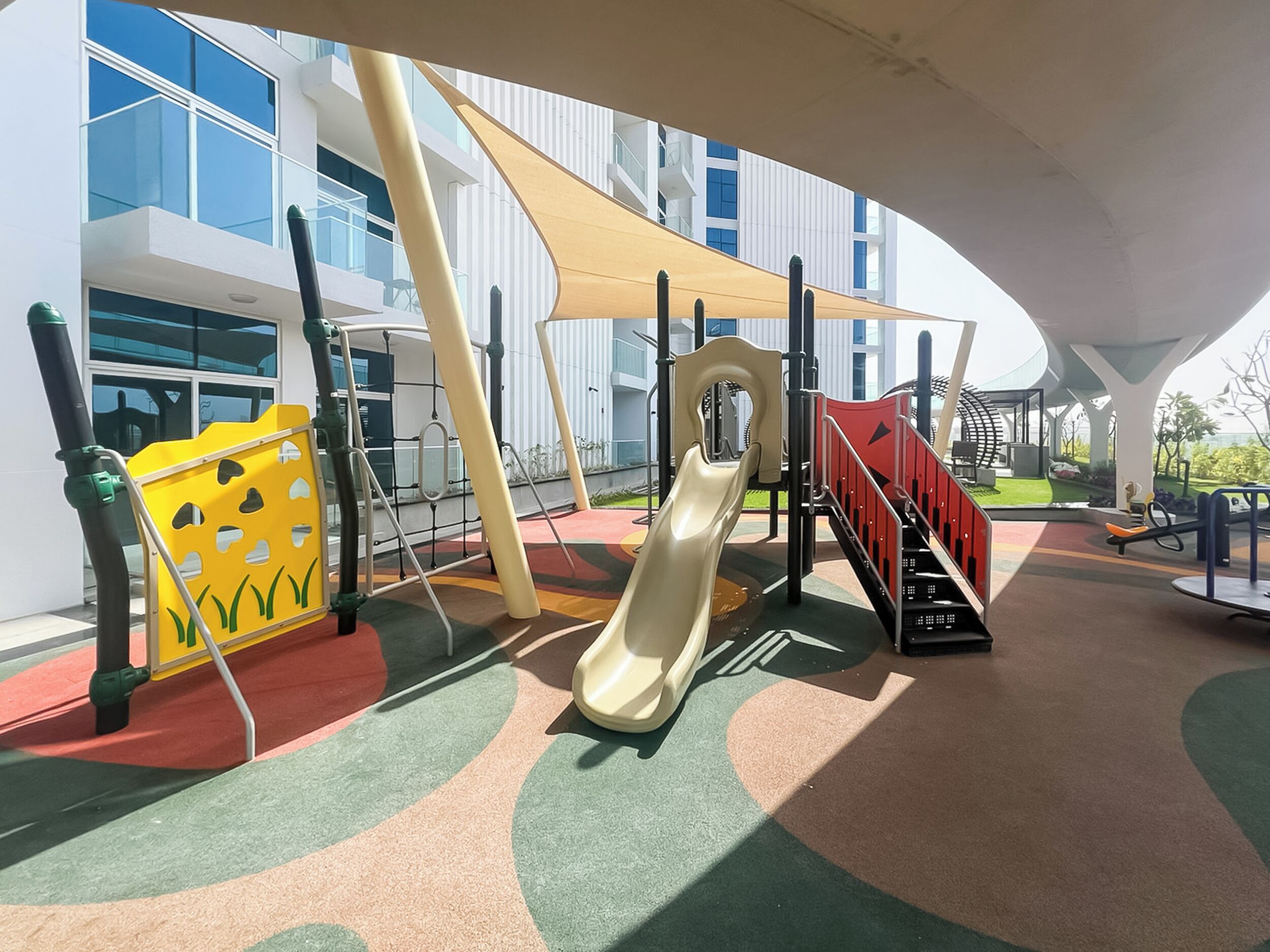 Un terrain de jeux équipé de toboggans et de structures d’escalade, entouré d’un bâtiment moderne doté de grandes fenêtres.