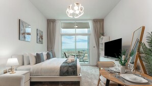 Une chambre d’hôtel moderne avec un grand lit, une table à manger dressée pour deux personnes, une télévision et un balcon offrant une vue sur la ville.