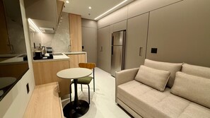 A modern kitchen with a built-in refrigerator, a dining area with a round table and chairs, and a sofa in the living area. - Modern Studio Alphaville (Barueri)