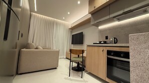 A modern kitchen with a built-in oven, a dining area with a chair, and a sofa. - Modern Studio Alphaville (Barueri)